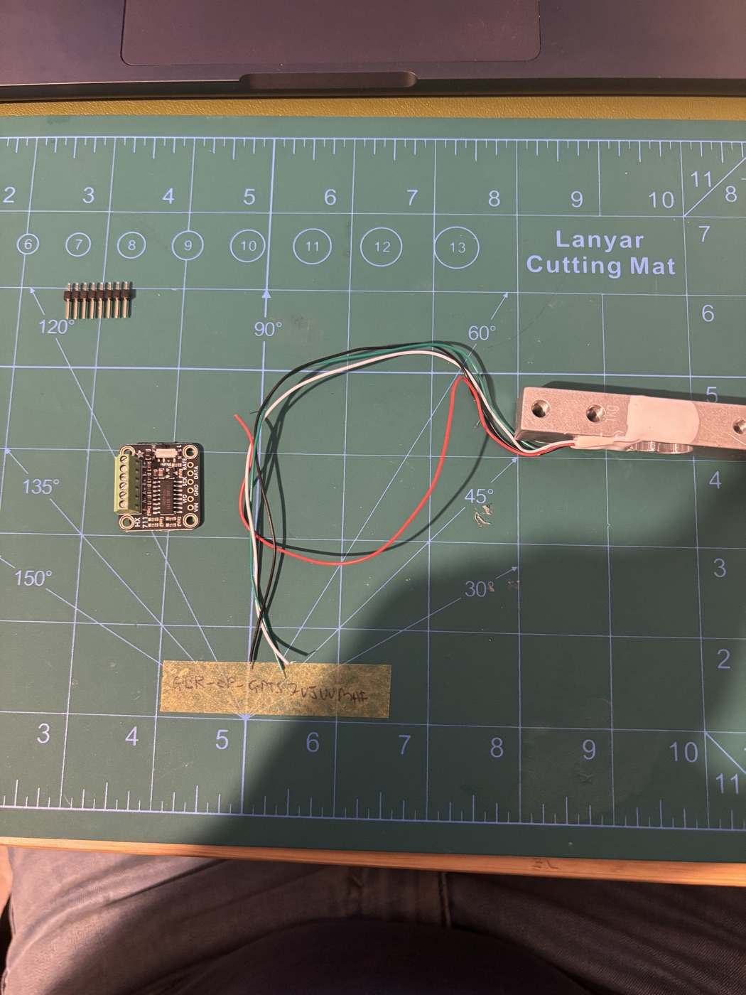 The HX711 board, the load cell and its four wires laid out on a cutting mat