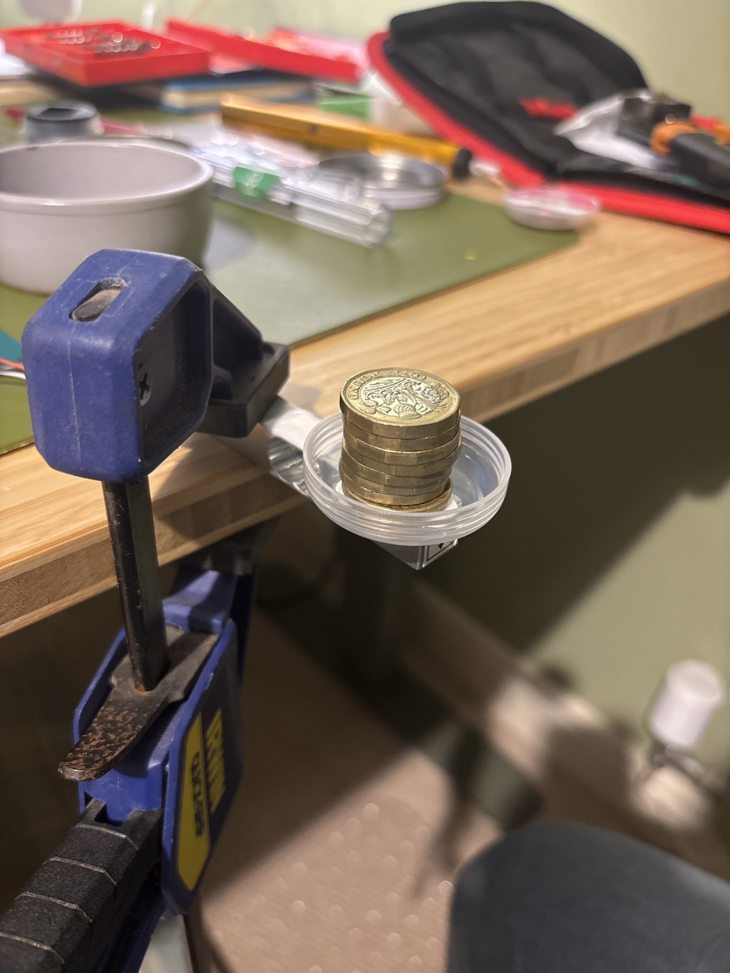 The load cell clamped to a bench edge with a lid on its free end holding a stack of eight pound coins