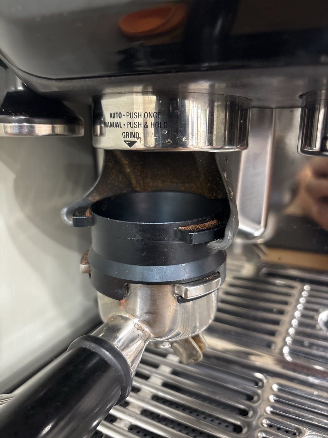 The dosing ring hanging on the cradle's hooks under the grinder outlet, with the portafilter clipped underneath
