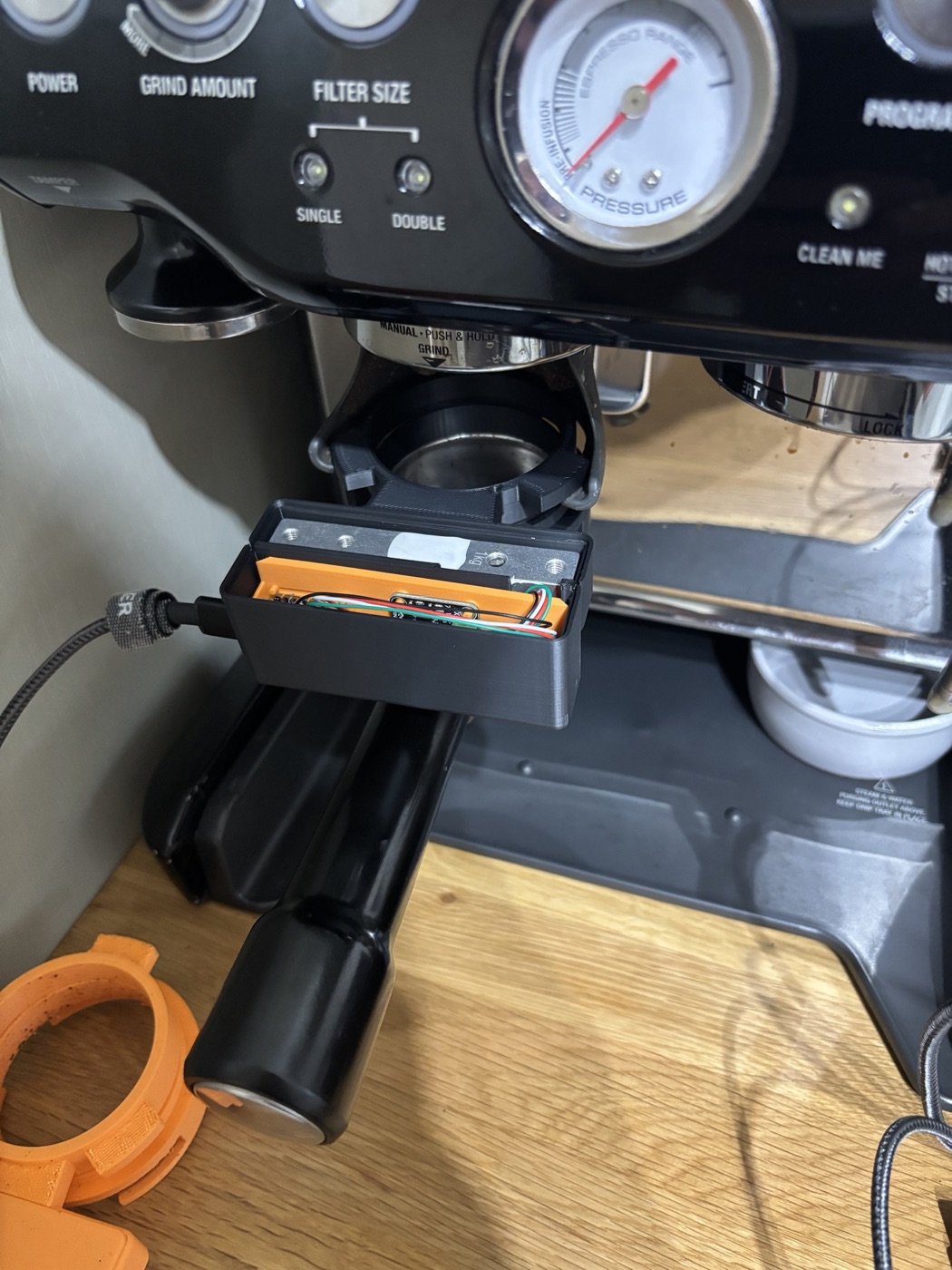 The assembled ring hanging in the cradle with the lid off, load cell and orange carrier visible, USB lead in, the portafilter handle below