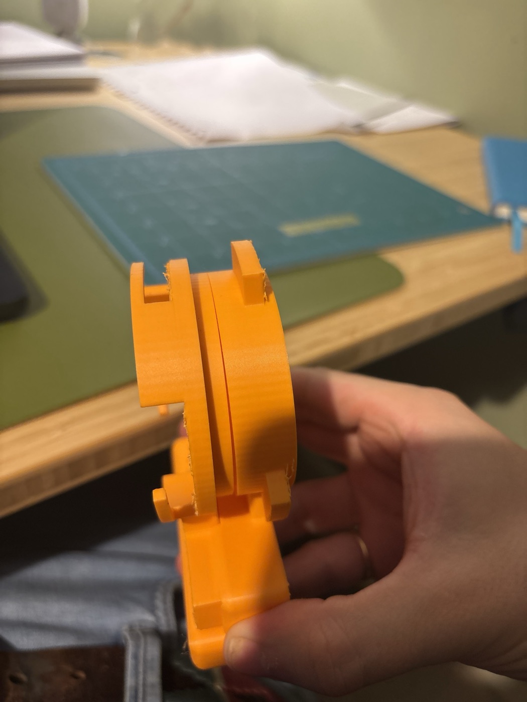 A hand holding the orange printed halves glued together with a stand-in load cell, the gap between them barely visible